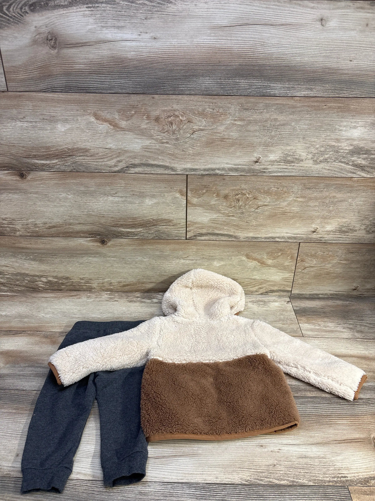 Flat lay of Little Me 2pc faux fur hooded jacket and pants showcasing cream and brown jacket and charcoal pants on wood