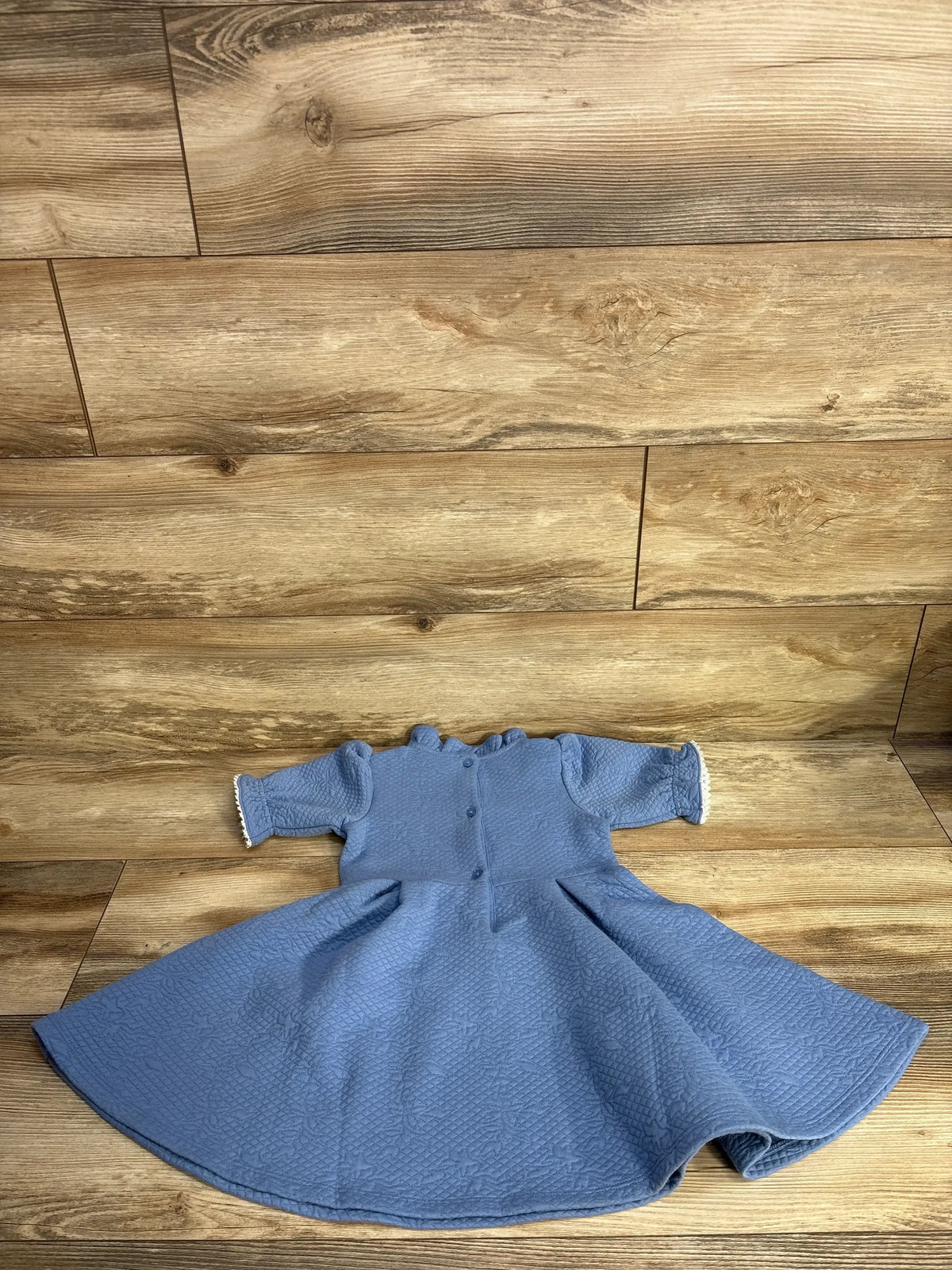 Flat lay of Janie and Jack pale blue ruffle jacquard dress 3T showing quilted texture, button back and lace cuffs on wood