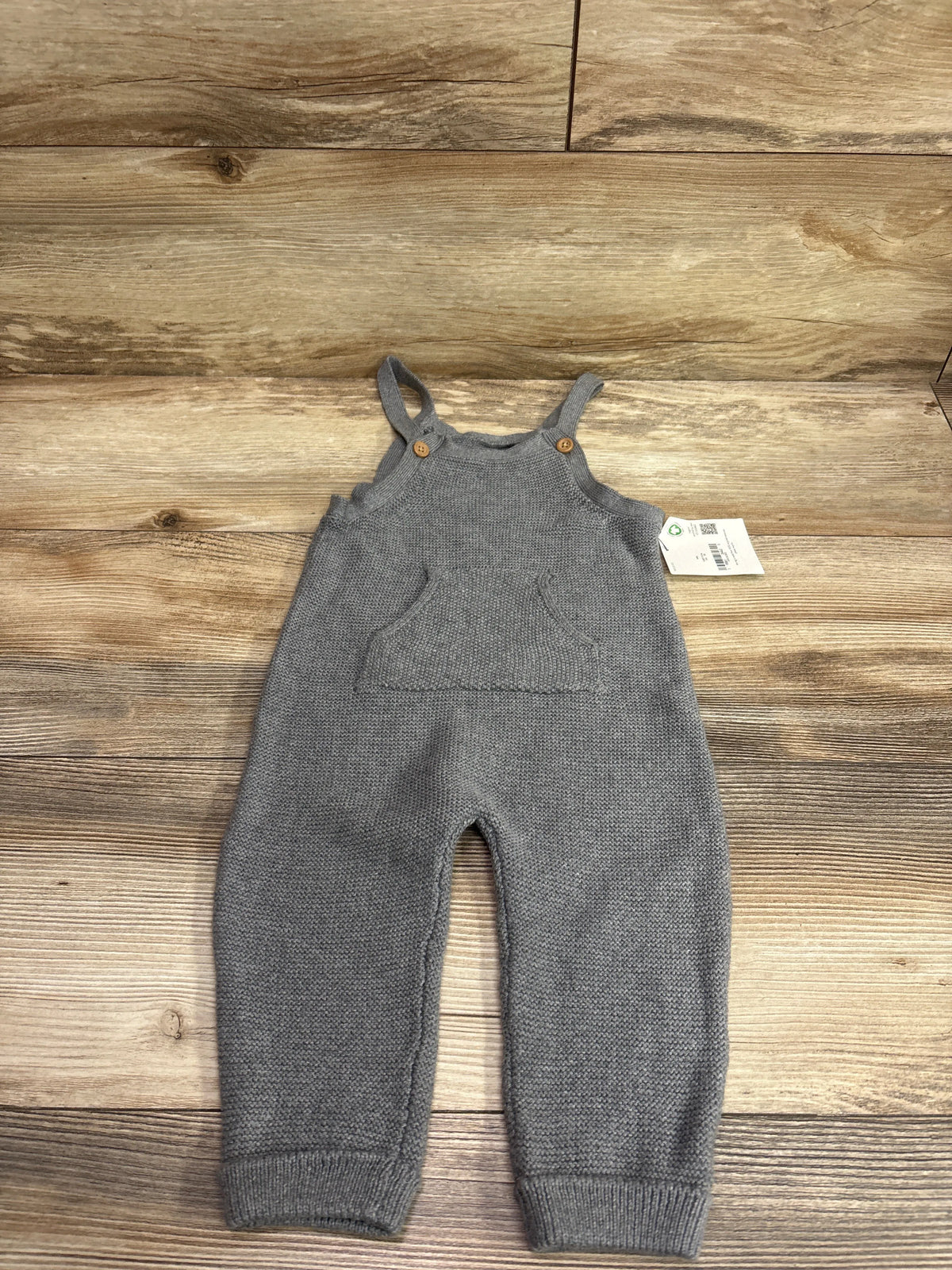 Front view of Little Planet gray knit overalls in size 12 months showcasing buttoned straps, front pocket, and ribbed cuffs on wood background