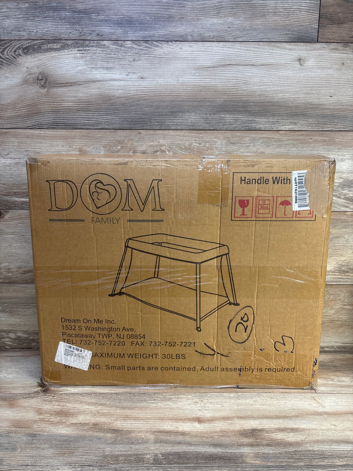 Front view of boxed Dream On Me Travel Light playard in blue showing printed product outline, handling icons and shipping labels on wooden floor