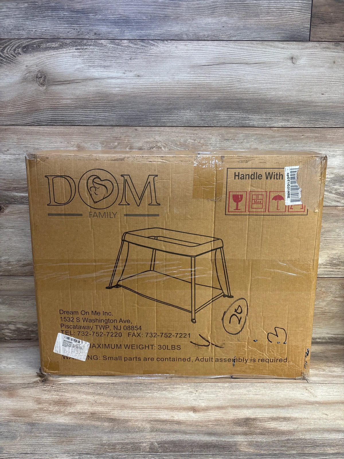 Front view of boxed Dream On Me Travel Light playard in blue showing printed product outline, handling icons and shipping labels on wooden floor