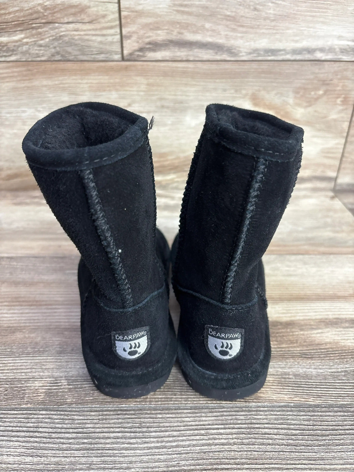 Pair of black Bearpaw children's boots with stitching detail on wooden floor