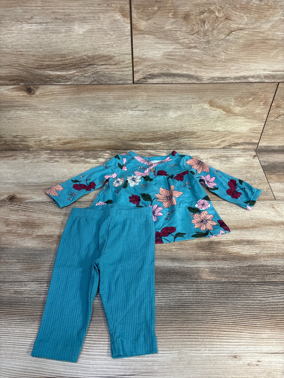 Top view of Carter’s blue henley shirt and pants set showcasing floral print and ribbed pants on a wood background