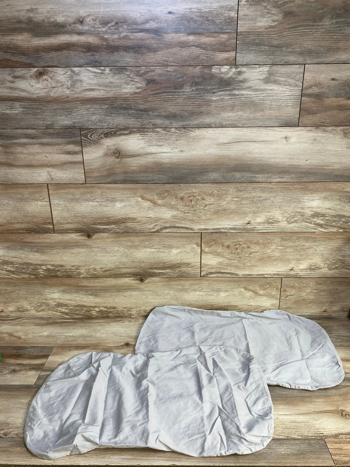 Flat lay of TILLYOU 2pk Baby Bassinet Sheets Grey showcasing two fitted oval sheets stacked on wood plank floor