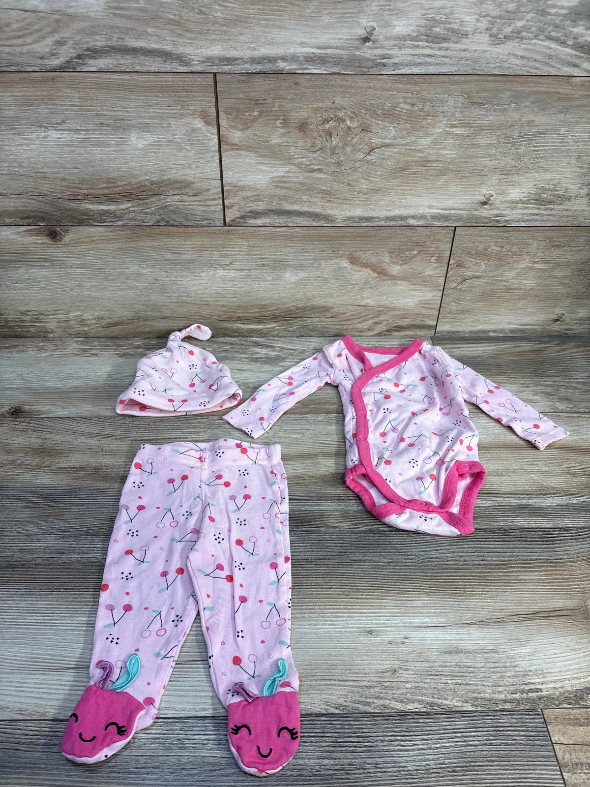 Top view of Koala Baby pink three-piece kimono shirt set with patterned bodysuit, footed pants, and knot hat on wood surface