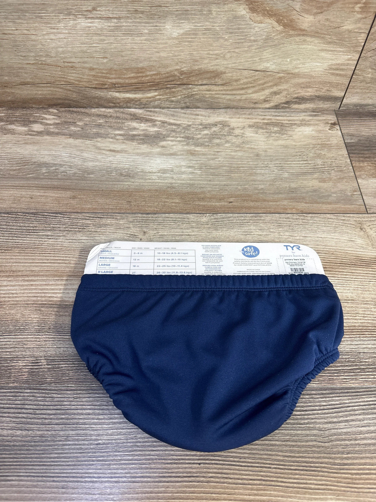 Flat lay of navy Pottery Barn swim diaper, size medium 12m, elastic waist and leg gathers on wood background
