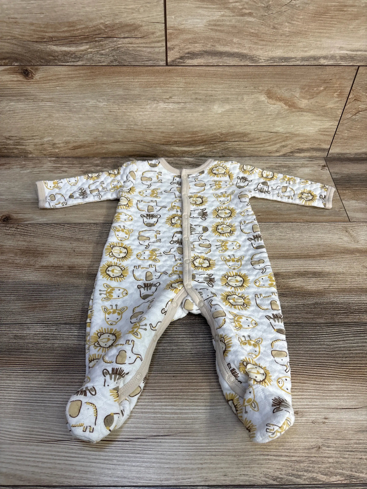 Front view of Little Beginnings white quilted footie sleeper with animal print on wood-grain background