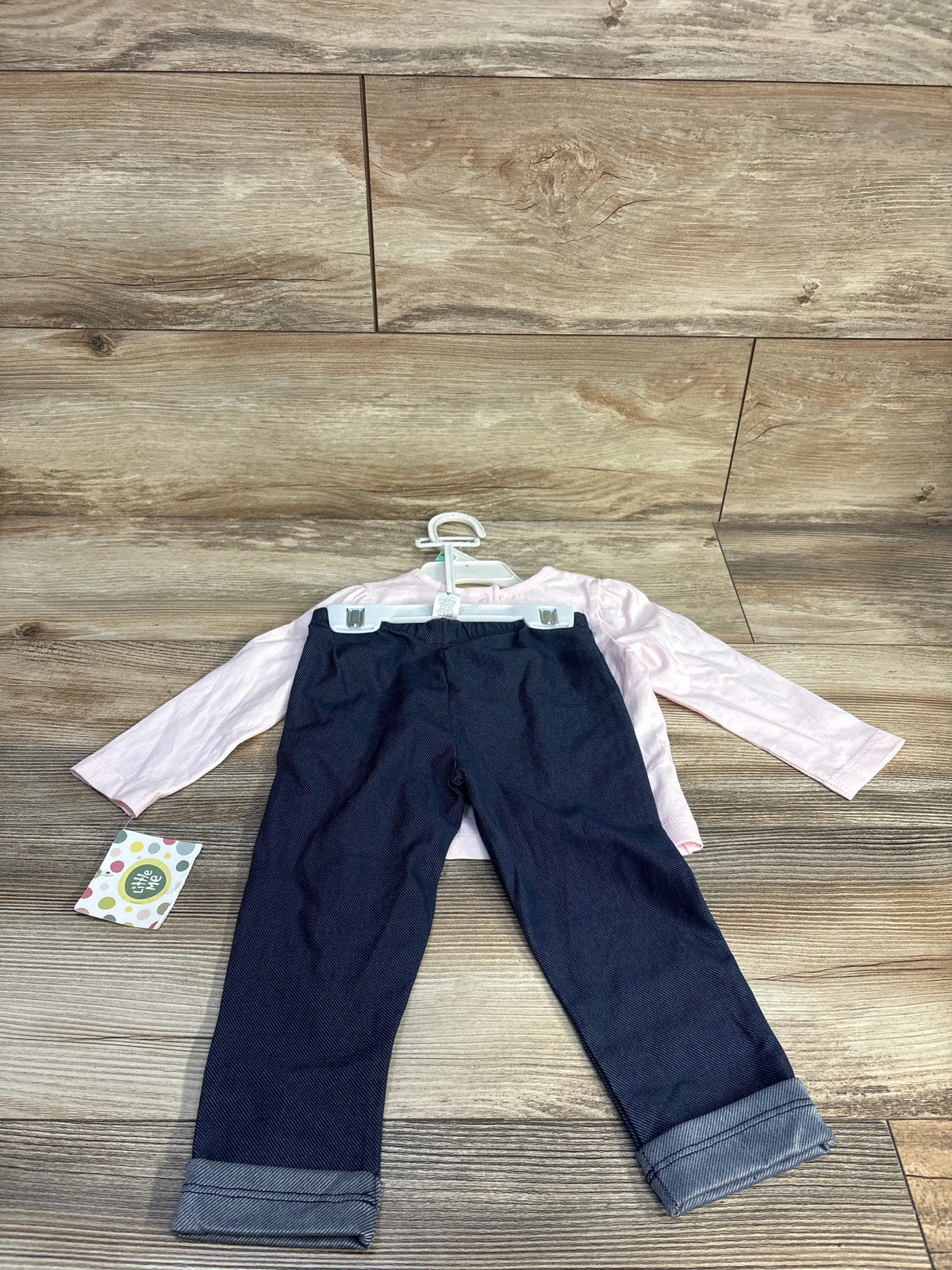Front view of Little Me two-piece shirt and jeggings set showcasing a pink long sleeve shirt and dark cuffed jeggings on a wood background