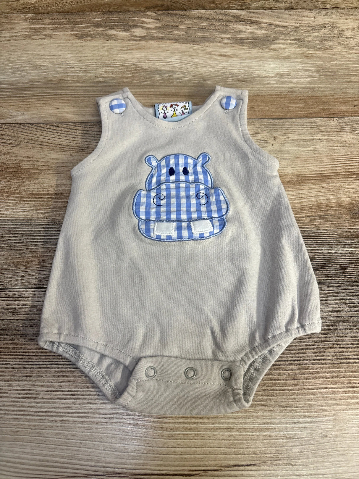 Flat lay of grey baby bubble romper with blue gingham hippo applique and button snaps at crotch on wood background