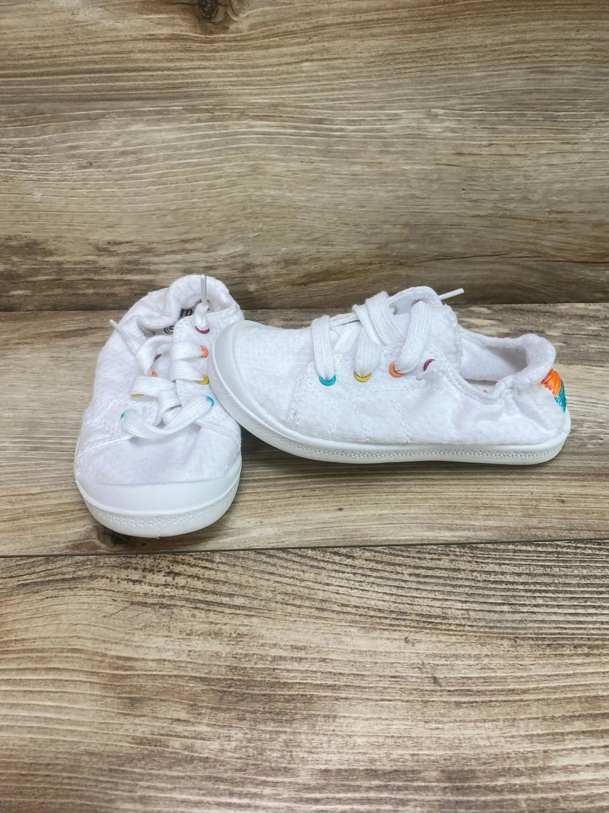 Side view of Wonder Nation Girls Casual Bump Toe Sneaker in white canvas with rainbow eyelets and slip-on laces on wood plank floor