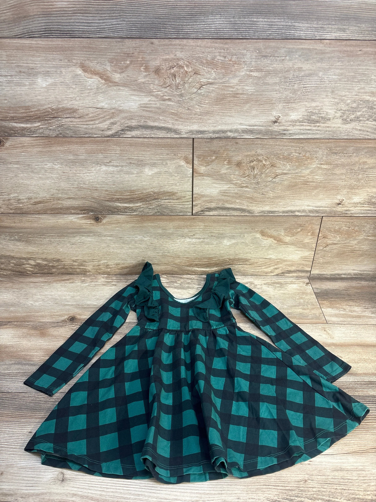 Girls long sleeve green and black plaid dress with ruffle detail on wooden floor