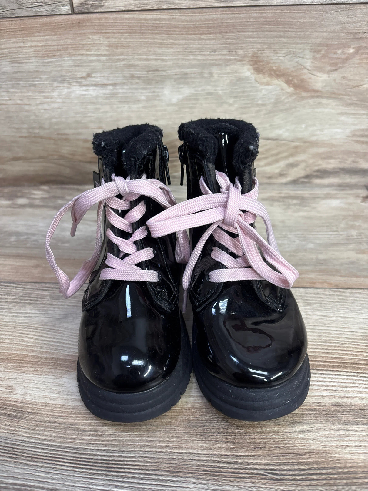 Pair of black shiny toddler boots with pink laces on wooden background