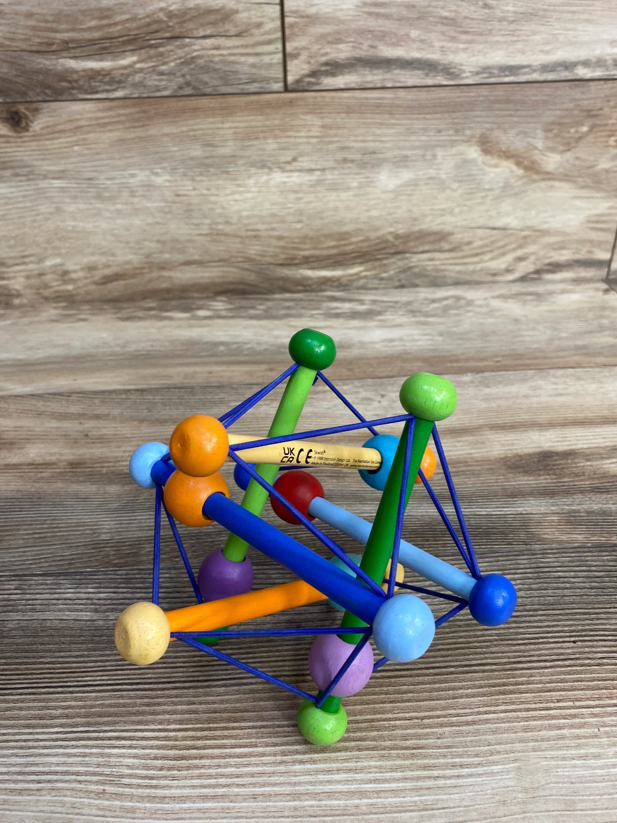 Colorful wooden baby toy with interconnected rods and elastic strings on wooden floor
