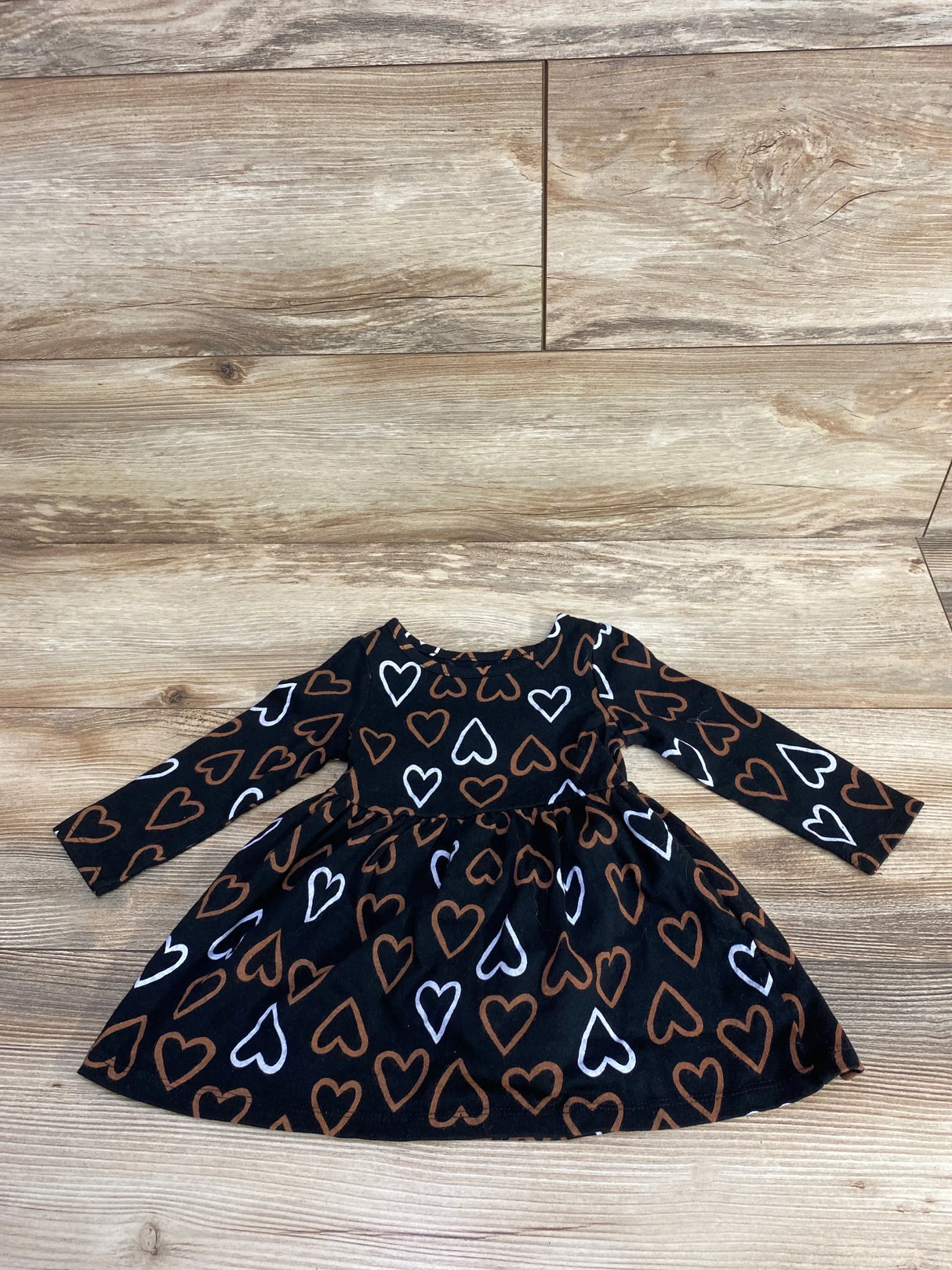 Long-sleeve black toddler dress with brown and white heart patterns on wooden floor