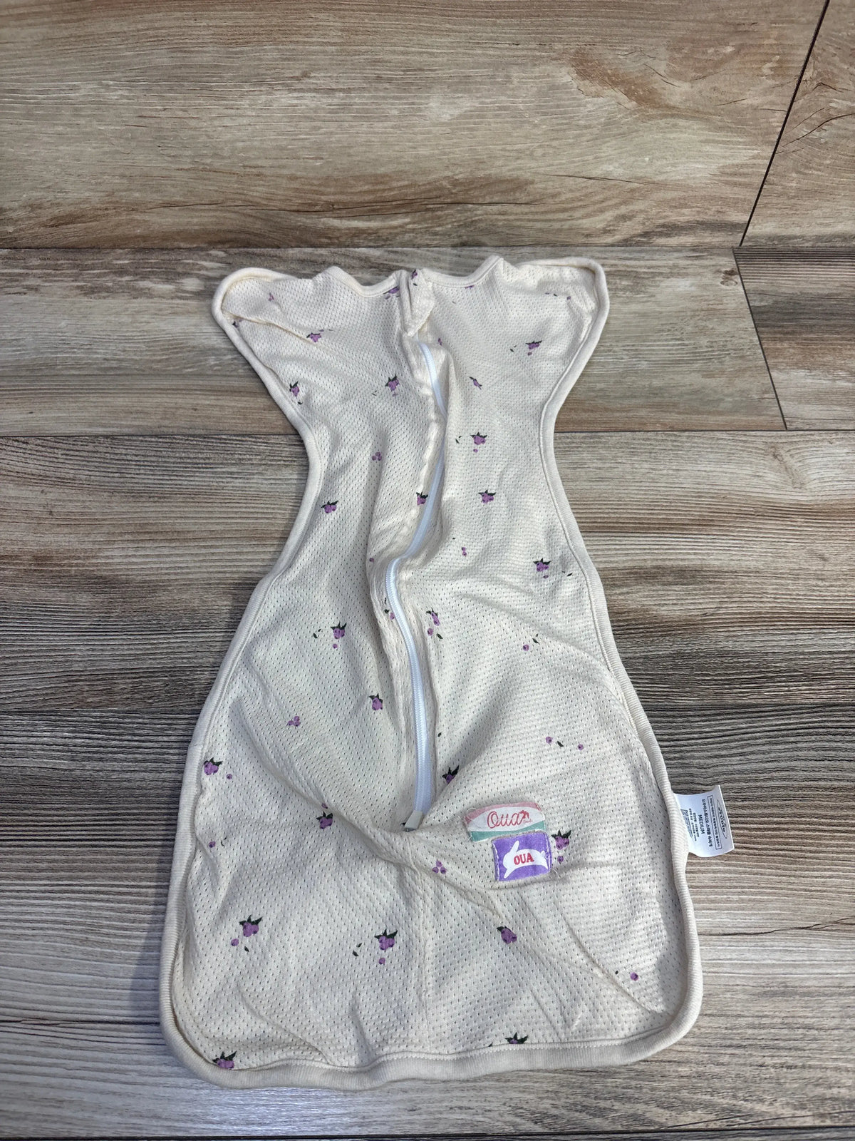 Front view of OUA Studio beige mesh swaddle sleep sack showcasing two-way zipper and purple print on wood background