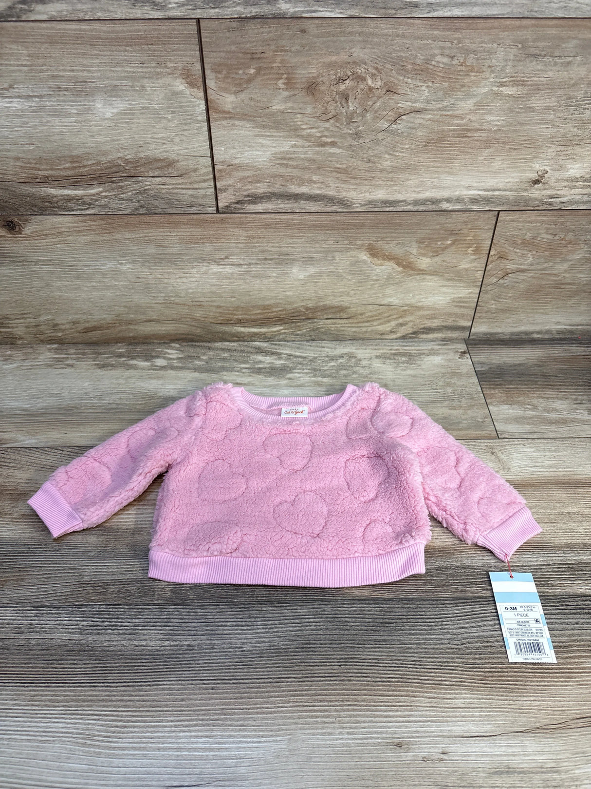 Pink fuzzy baby sweater with heart pattern, long sleeves, size 0-3 months, on wood floor
