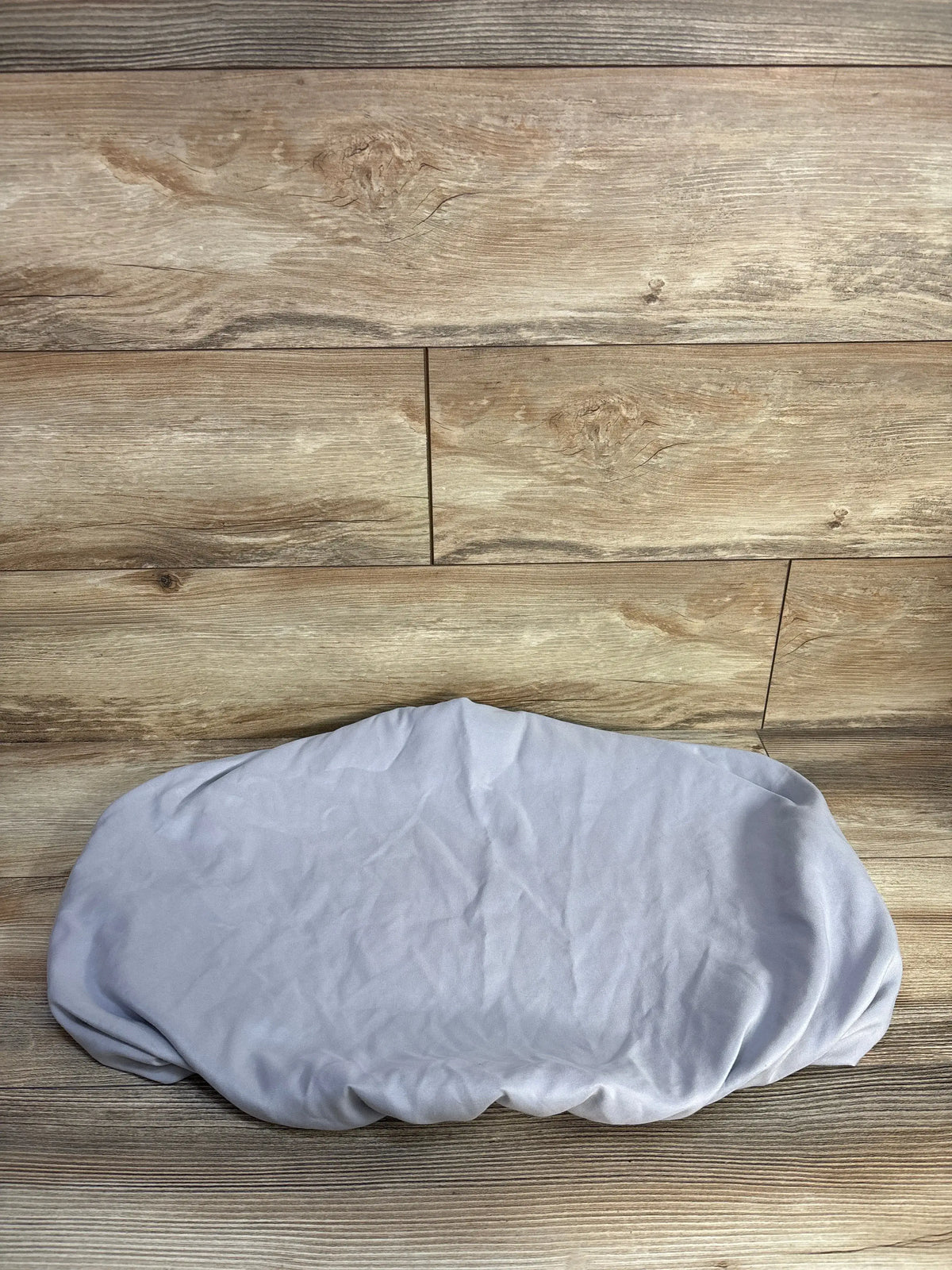 Top-down view of Parent’s Choice fitted bassinet sheet in light grey showing elasticized edges on wood-plank background
