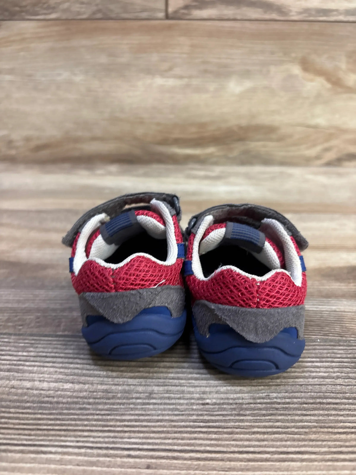 Rear of Pediped Gehrig Grip N Go toddler sneakers showing red mesh, gray suede heel, navy sole, Velcro strap on wood floor