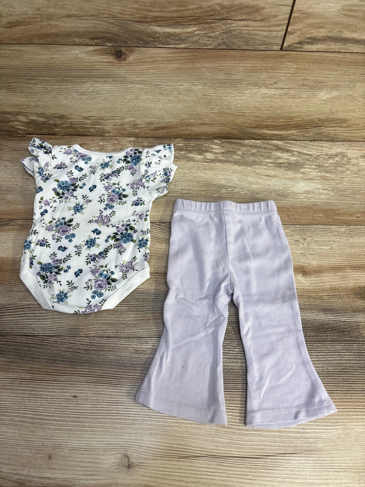 Floral baby onesie with ruffled sleeves and light purple bell-bottom pants on wooden floor