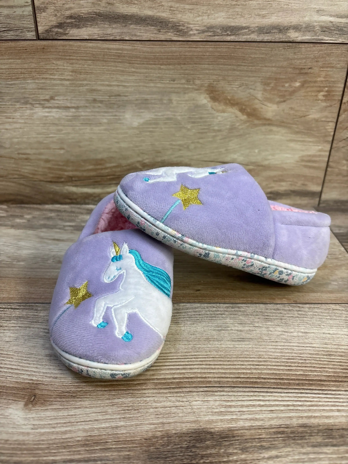 Angled front view of purple Wonder Nation toddler unicorn slippers with embroidered white unicorn, teal mane and gold star on wood background