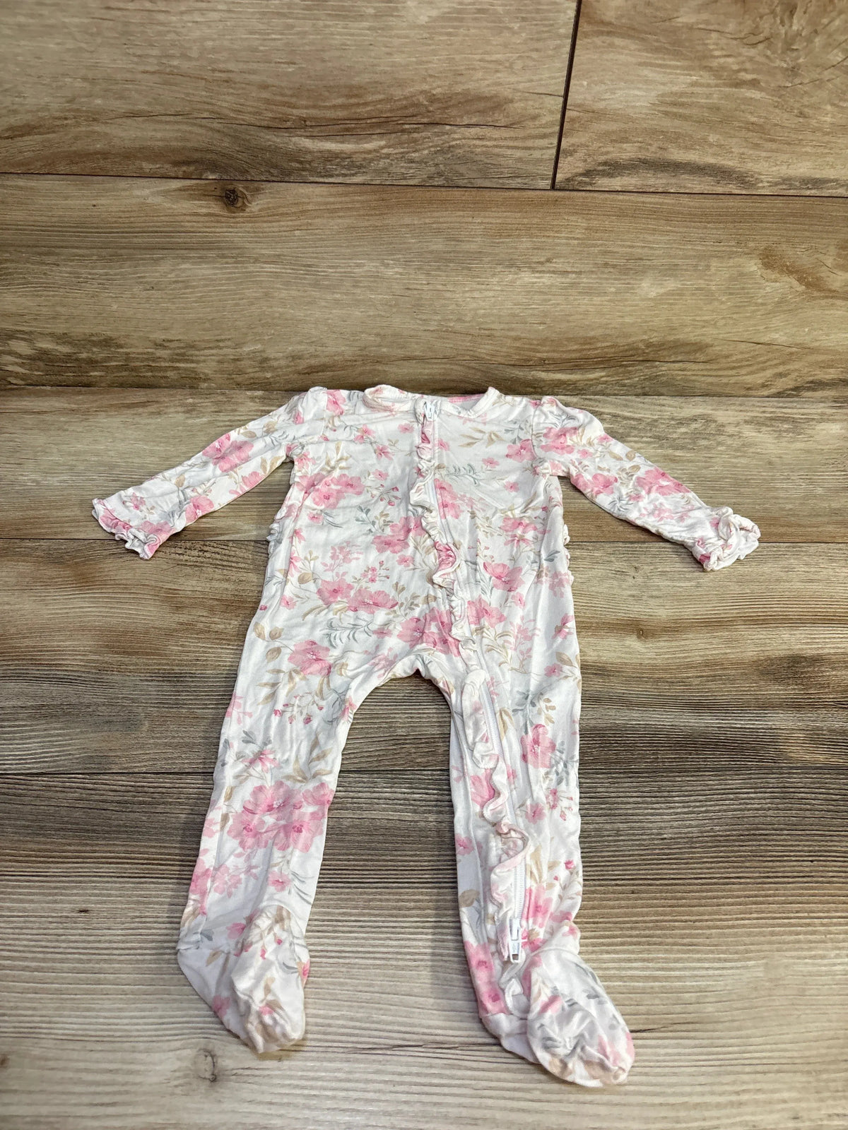 Flat lay of Little Me bamboo ruffle footed sleeper showcasing front zipper ruffle and pink floral print on wooden floor