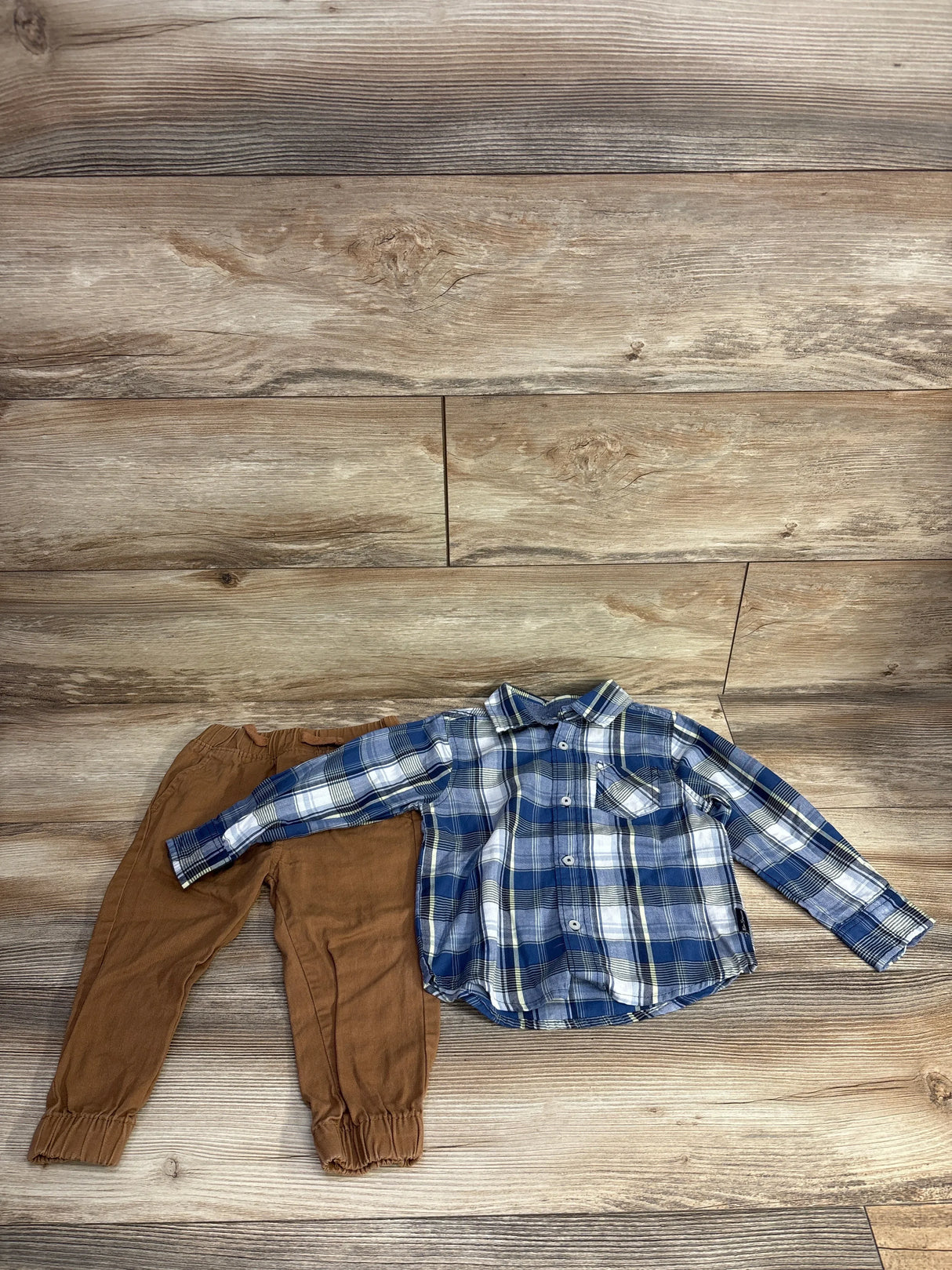 Boy's brown jogger pants with blue plaid long-sleeve shirt on wood background