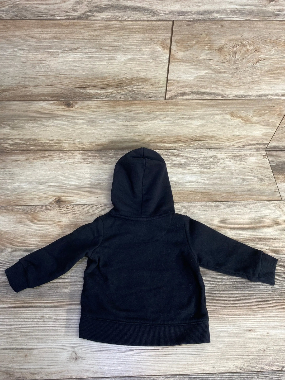Back view of Reebok pullover hoodie in black showcasing hood and ribbed cuffs on wood plank floor