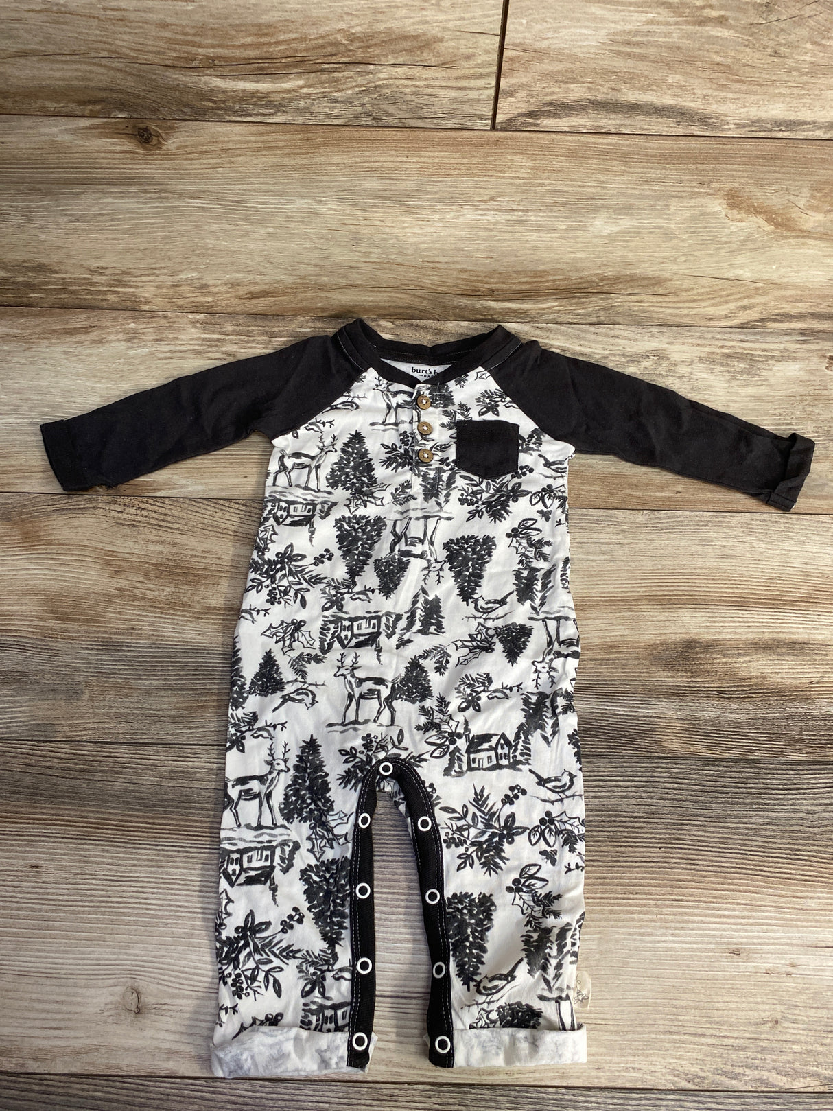 Black and white baby romper with deer and tree print, black sleeves, and buttons on wooden floor