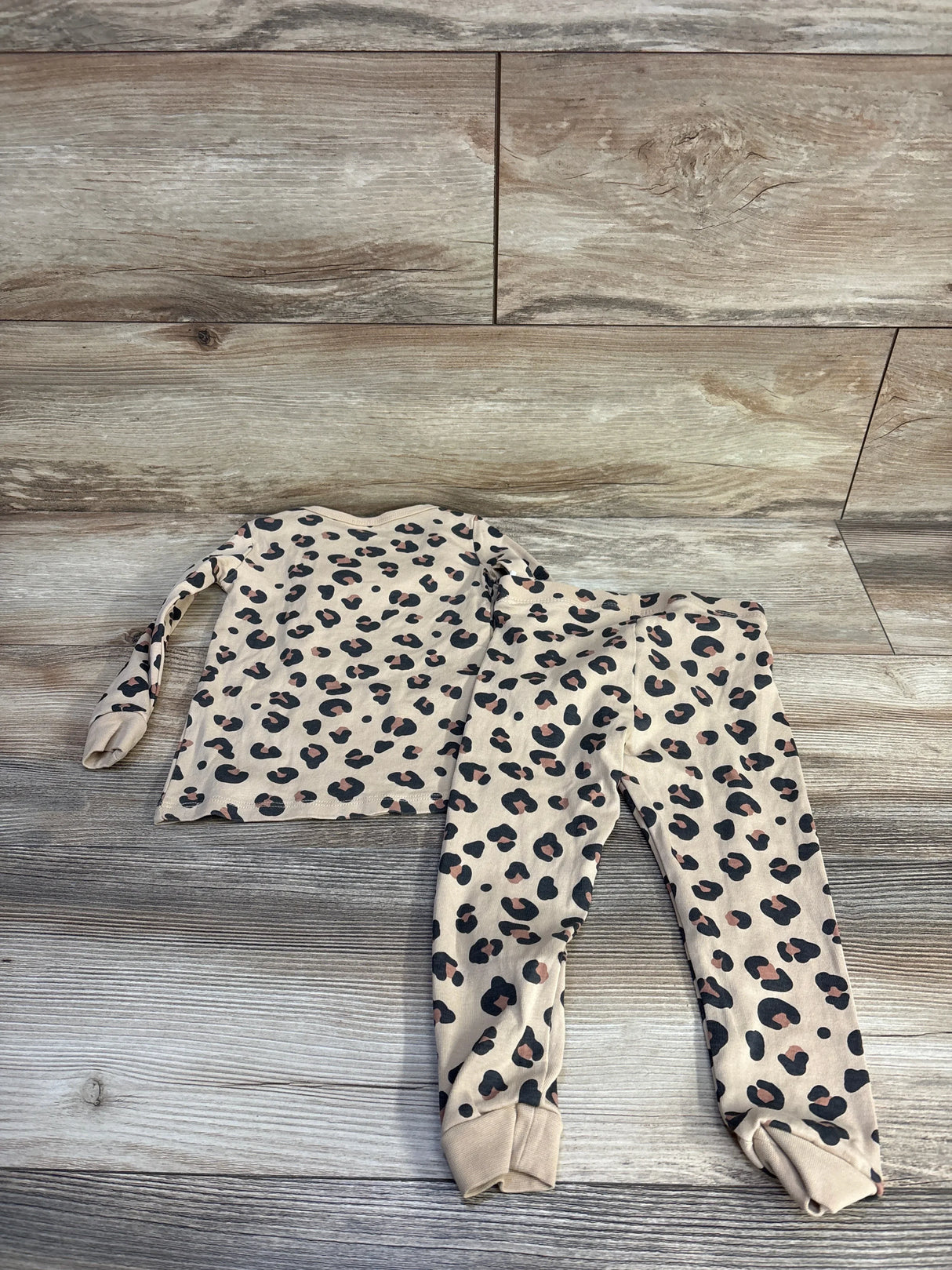 Top-down view of girls H&M 2-piece leopard print pajama set size 2T showing long-sleeve top and cuffed pants on wood background