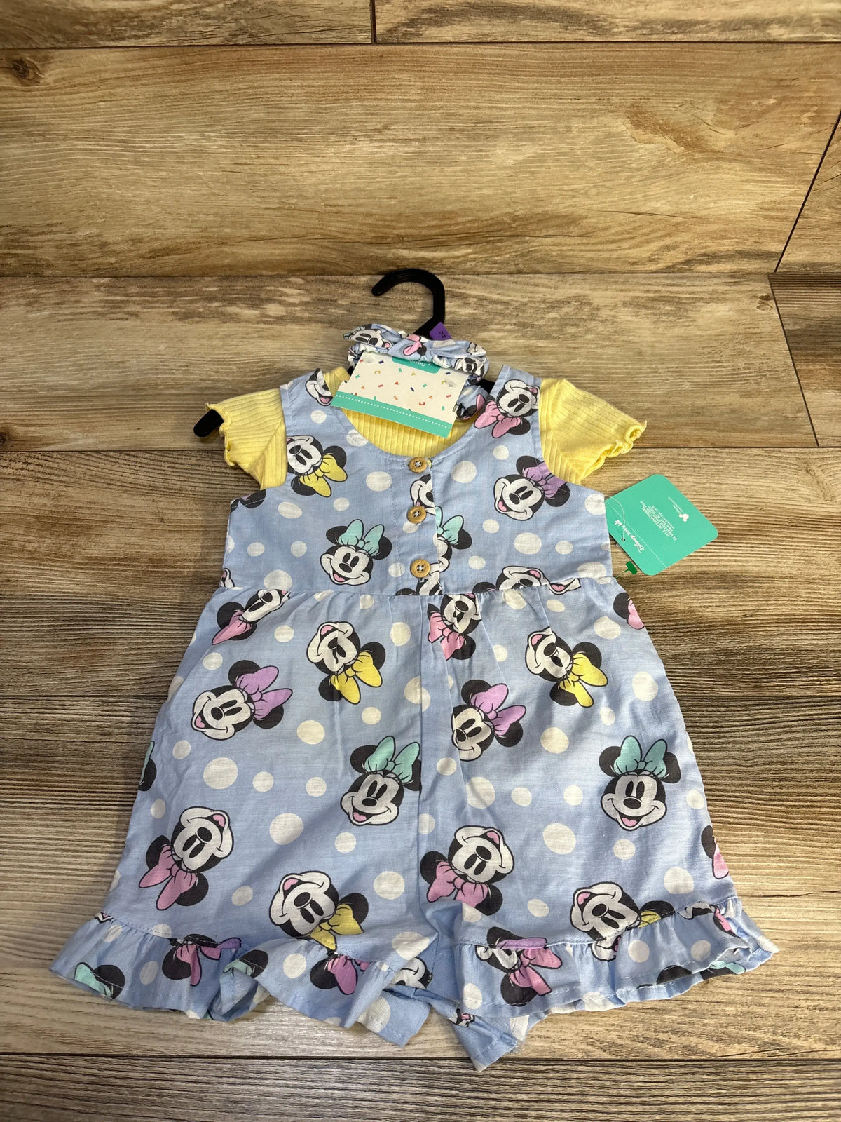 Flat lay of Disney Baby Minnie Mouse shortall set showcasing blue patterned shortalls, yellow ribbed shirt, and headband