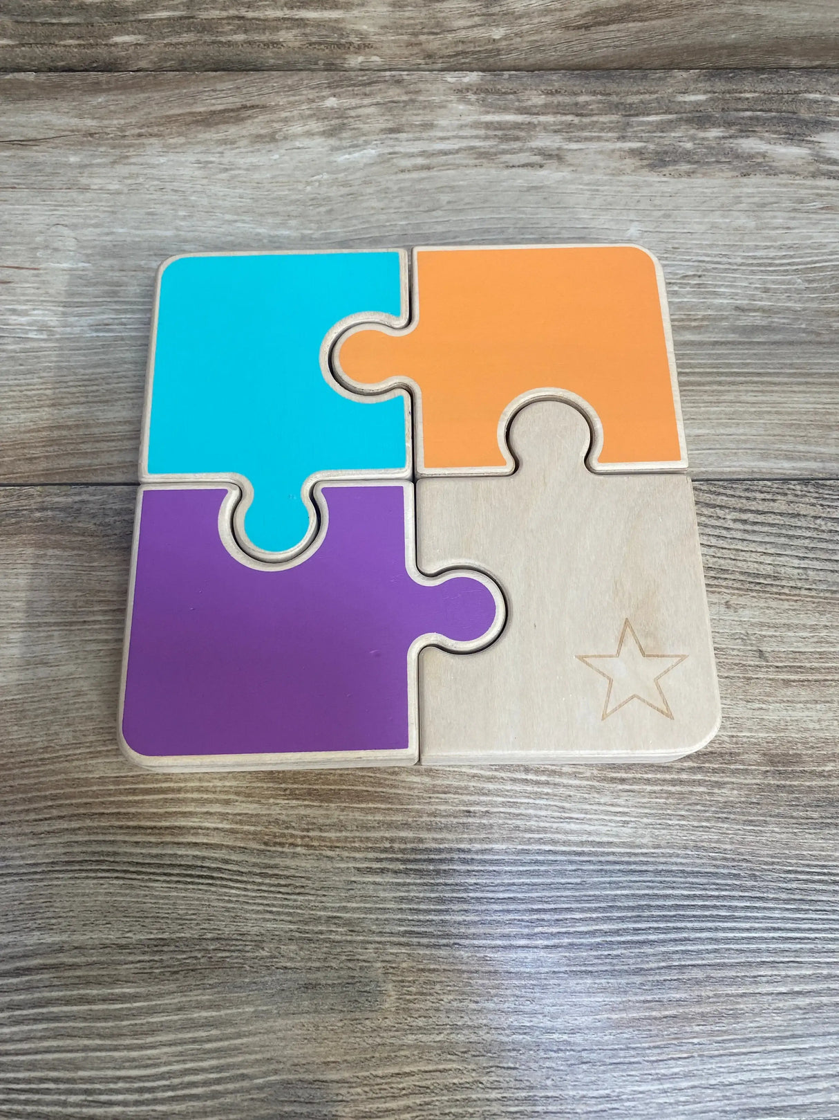Top view of Lovevery chunky jigsaw puzzle with four interlocking pieces (teal, orange, purple, natural) on woodgrain tabletop