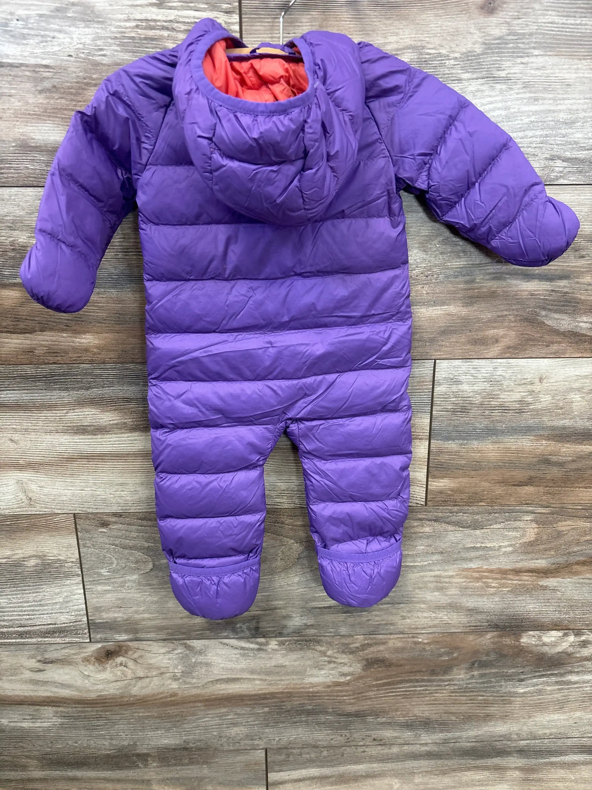 Purple insulated baby snowsuit with hood and mittens, laid flat on wood floor, for cold weather