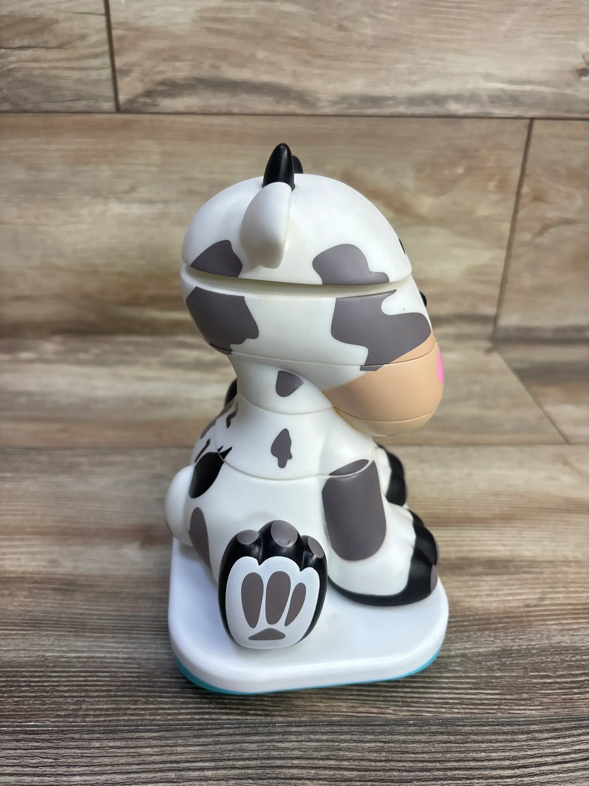 Side view of Stack-a-Roos Baby Cow stacking toy showcasing stacked cow-shaped rings, pink snout, and paw-print base on wood floor background