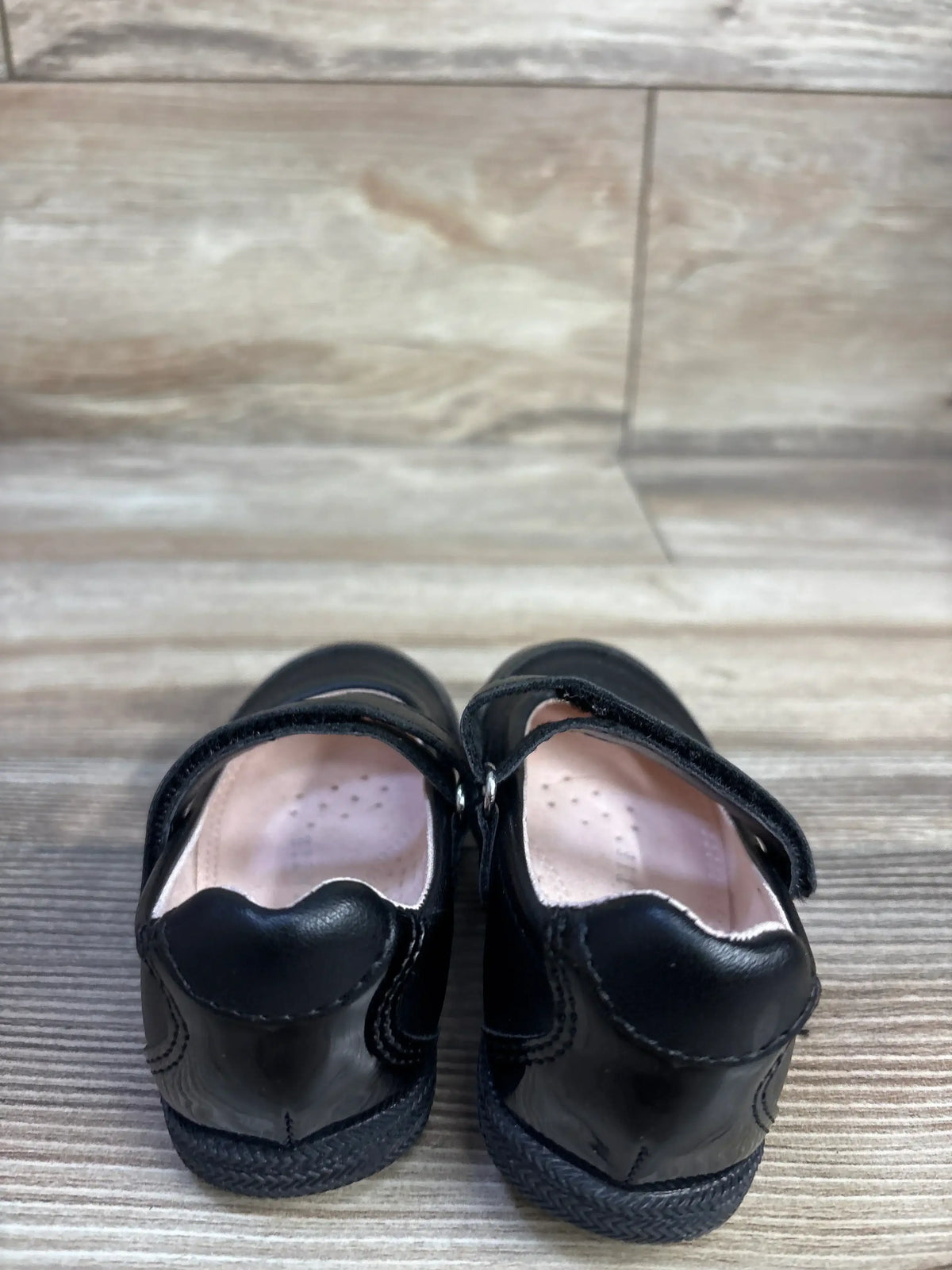 Back view of Kelly and Kate Francis black Mary Jane flats showing scalloped heel, strap, and pink insole on wood floor