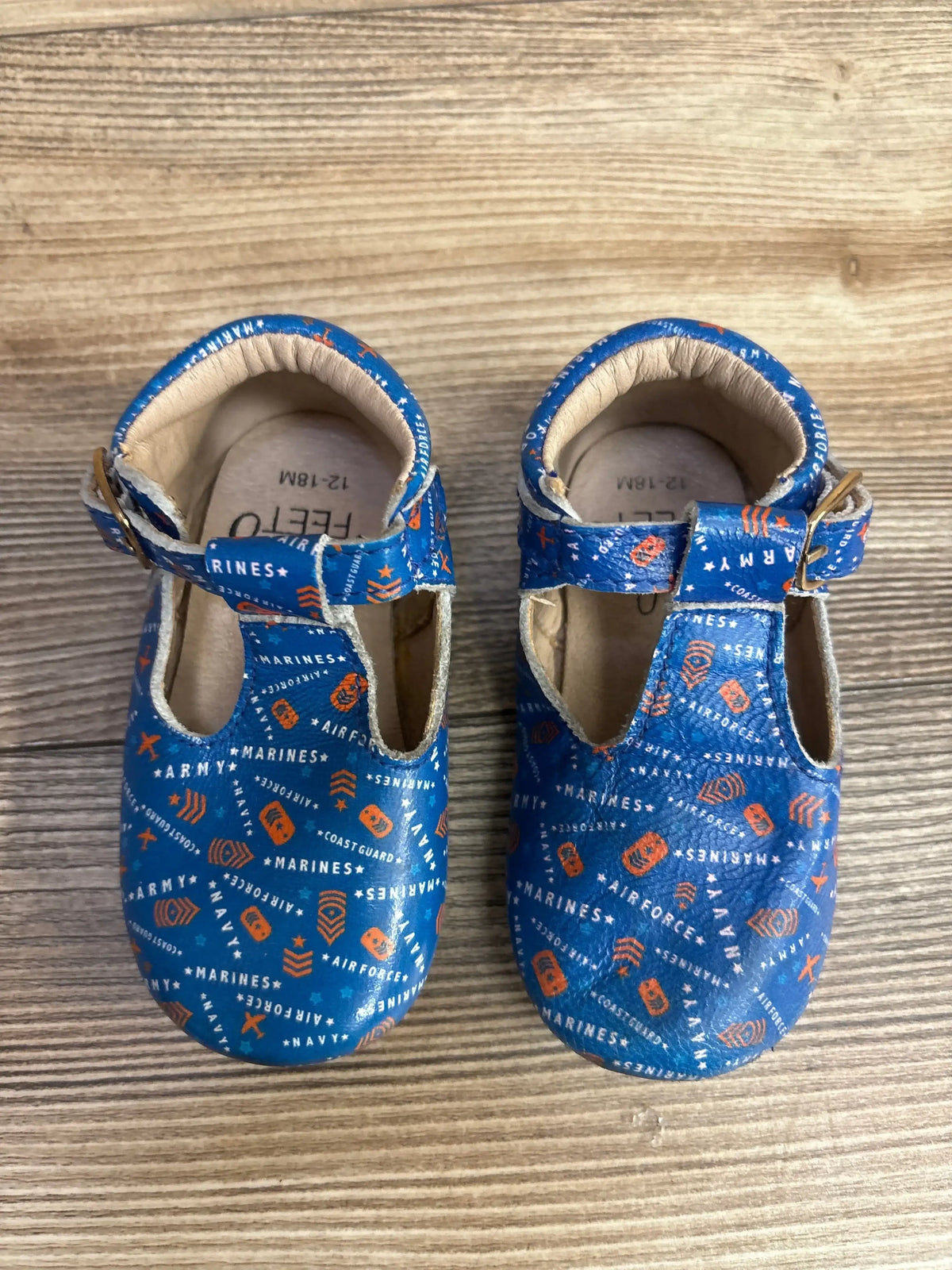 Blue baby shoes with military themed print, soft sole, buckle strap, on wood background