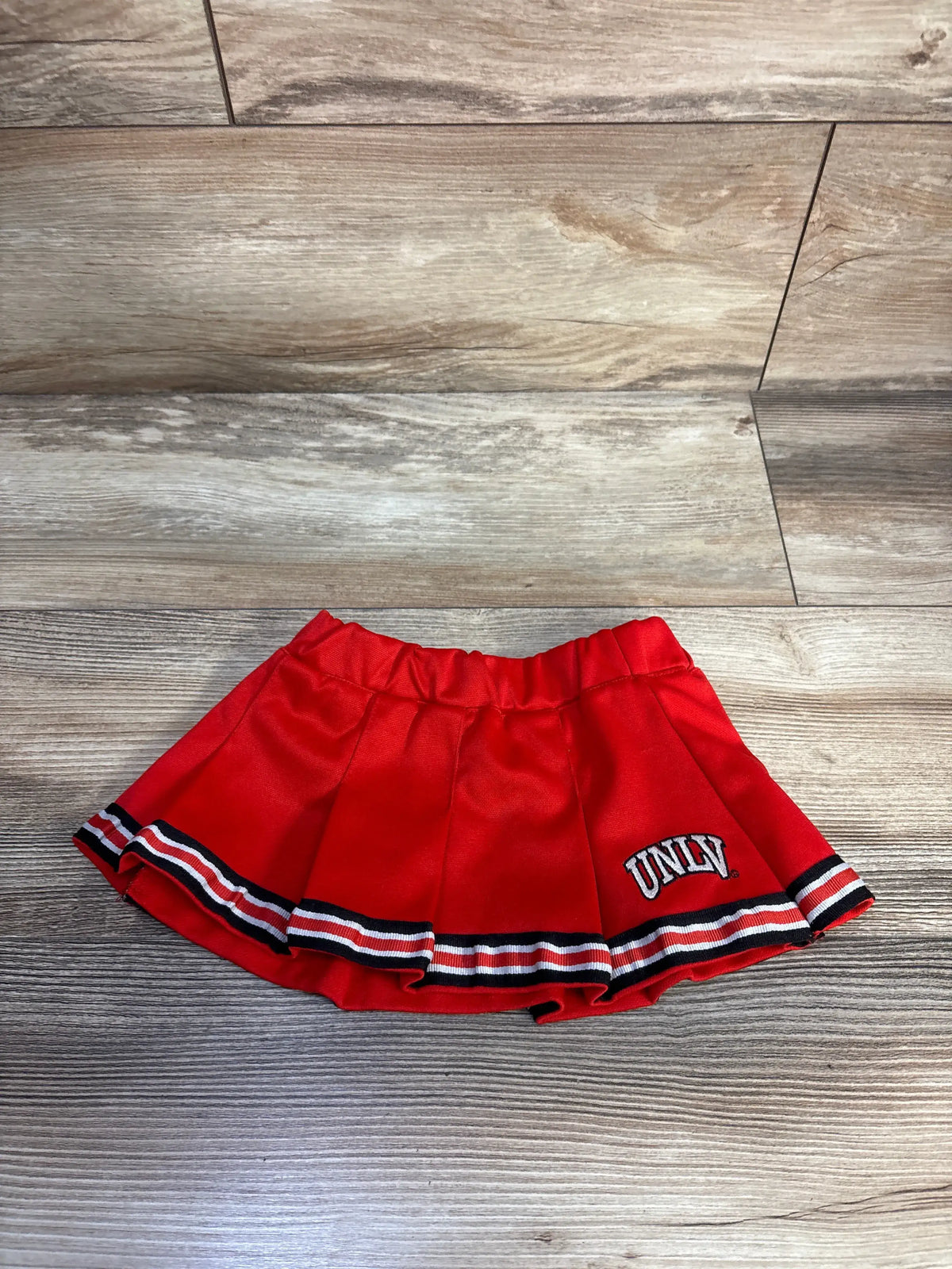 Front view of red NCAA UNLV skirt showcasing UNLV branding, elastic waistband, and striped trim on a wood floor