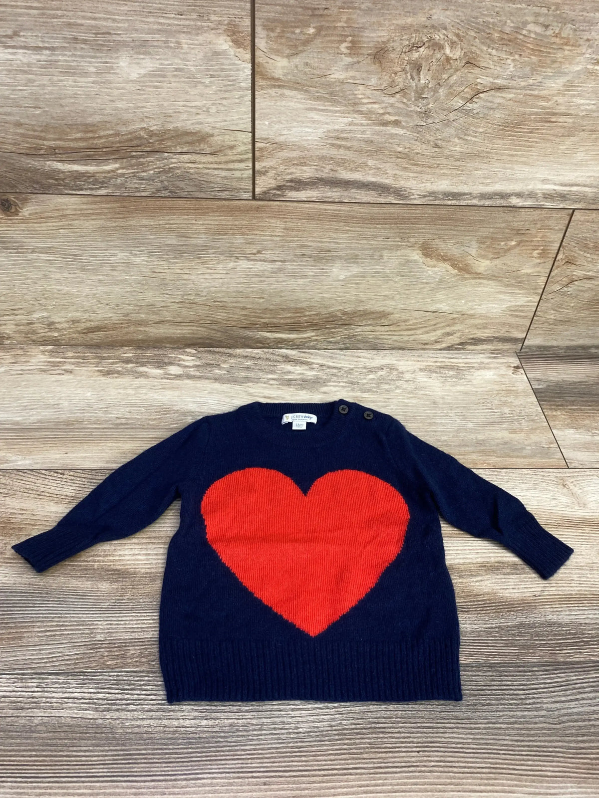 Navy blue baby sweater with large red heart design, wooden floor background
