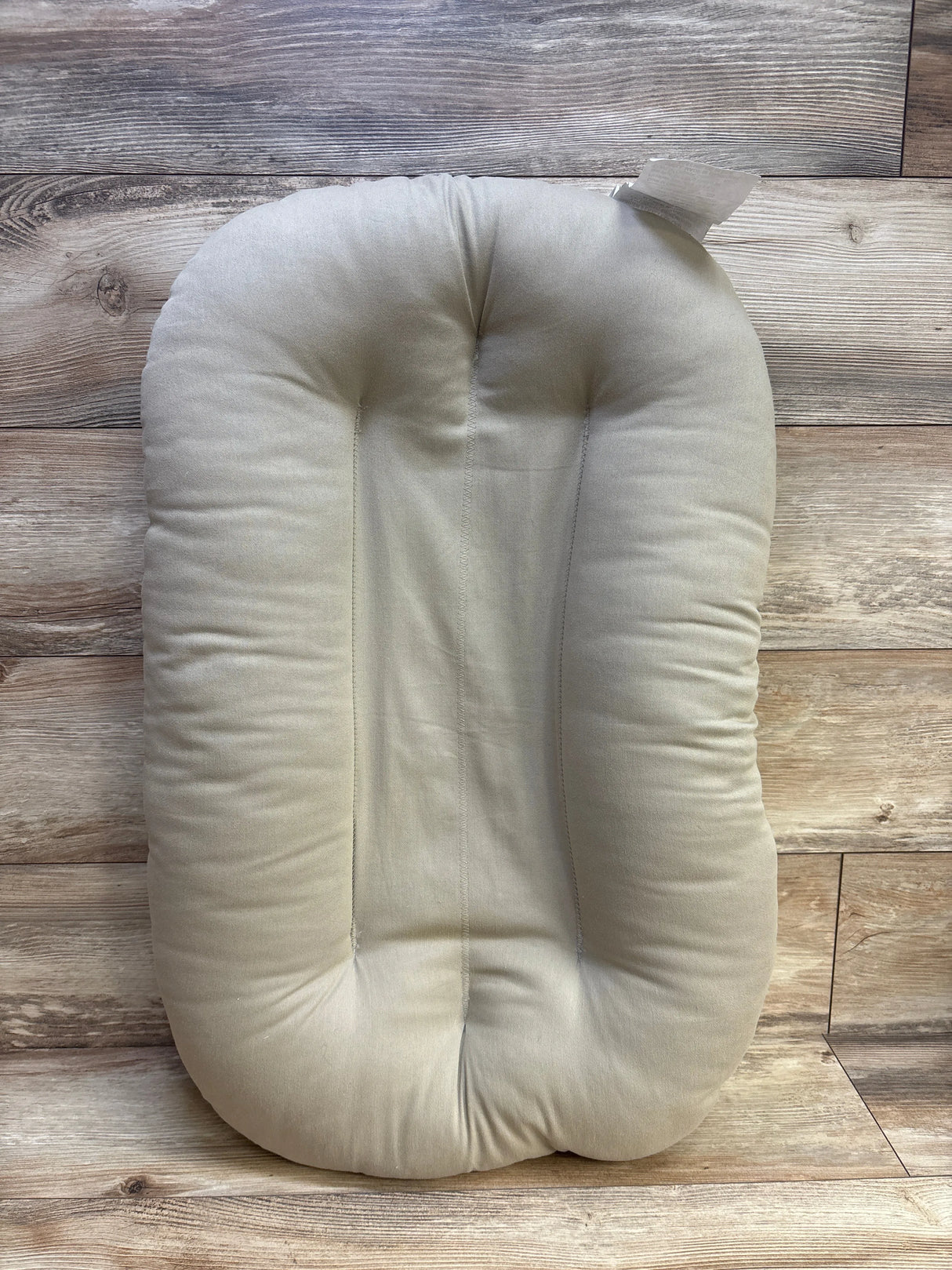 Beige oval baby lounger pillow on wooden floor background