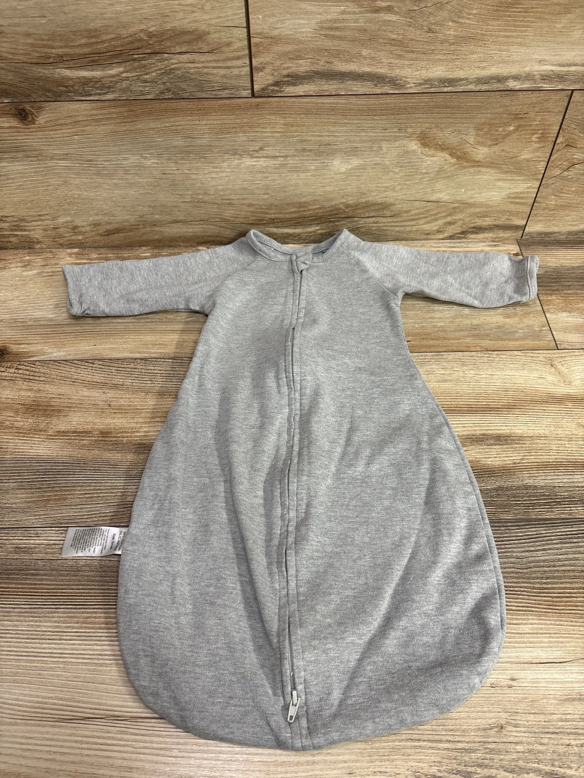Front view of gray long sleeve swaddle sack, size 0–6 months, showcasing full-length zipper and rounded bottom on wood floor