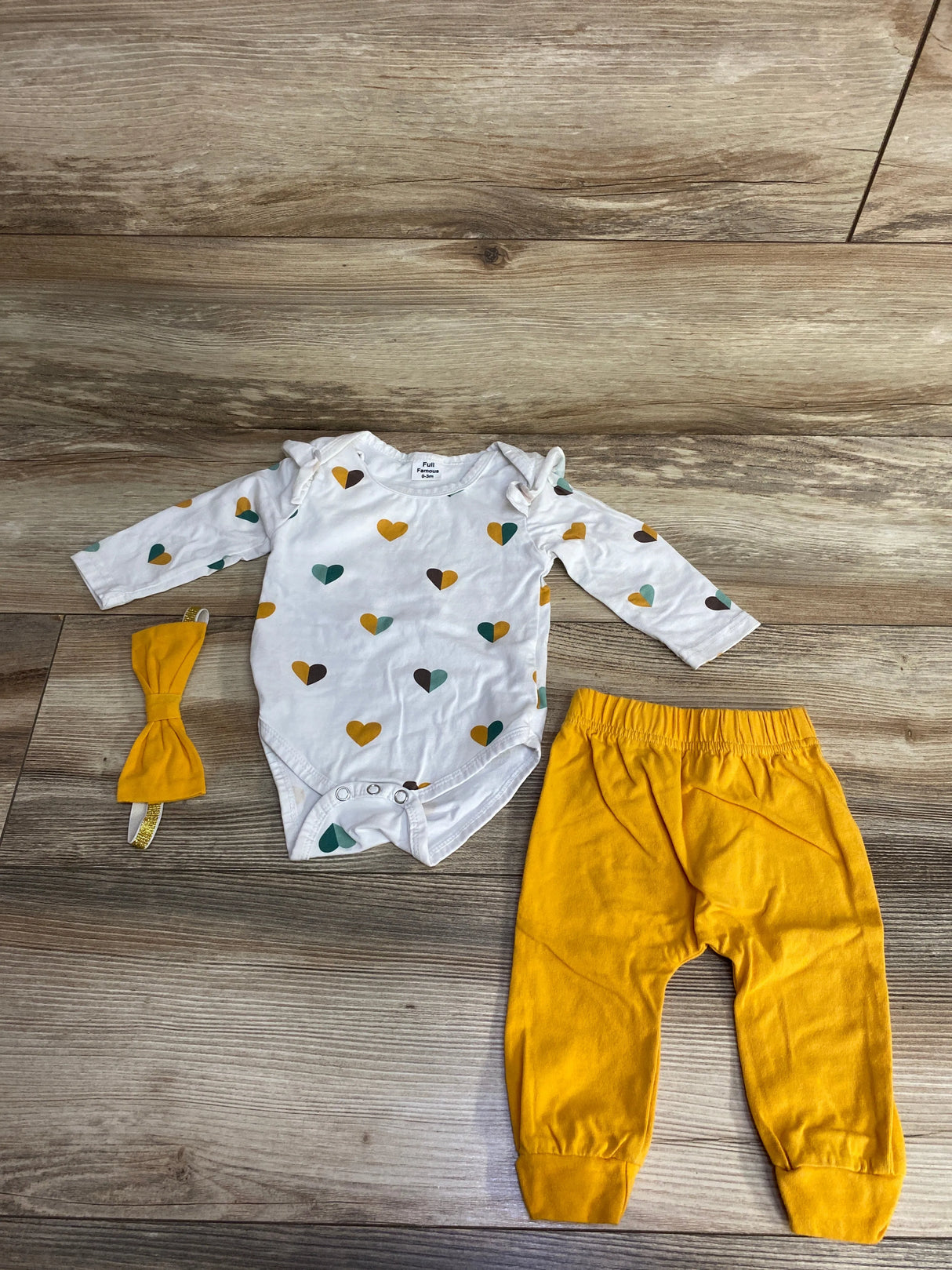 Baby outfit set with long-sleeve heart print onesie, mustard yellow pants, and matching headband on wooden floor