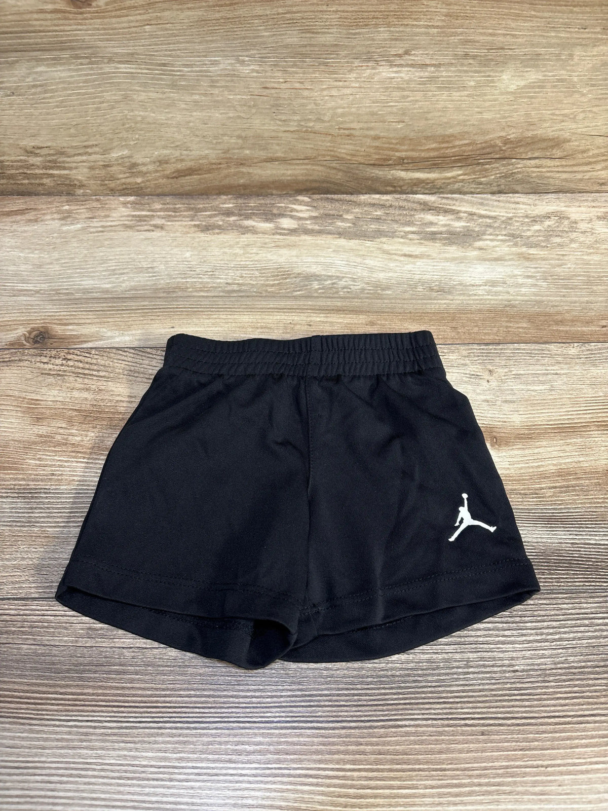 Flat lay of Jordan Active Shorts showcasing black fabric, elastic waistband, curved hem, and white Jumpman logo on wood grain