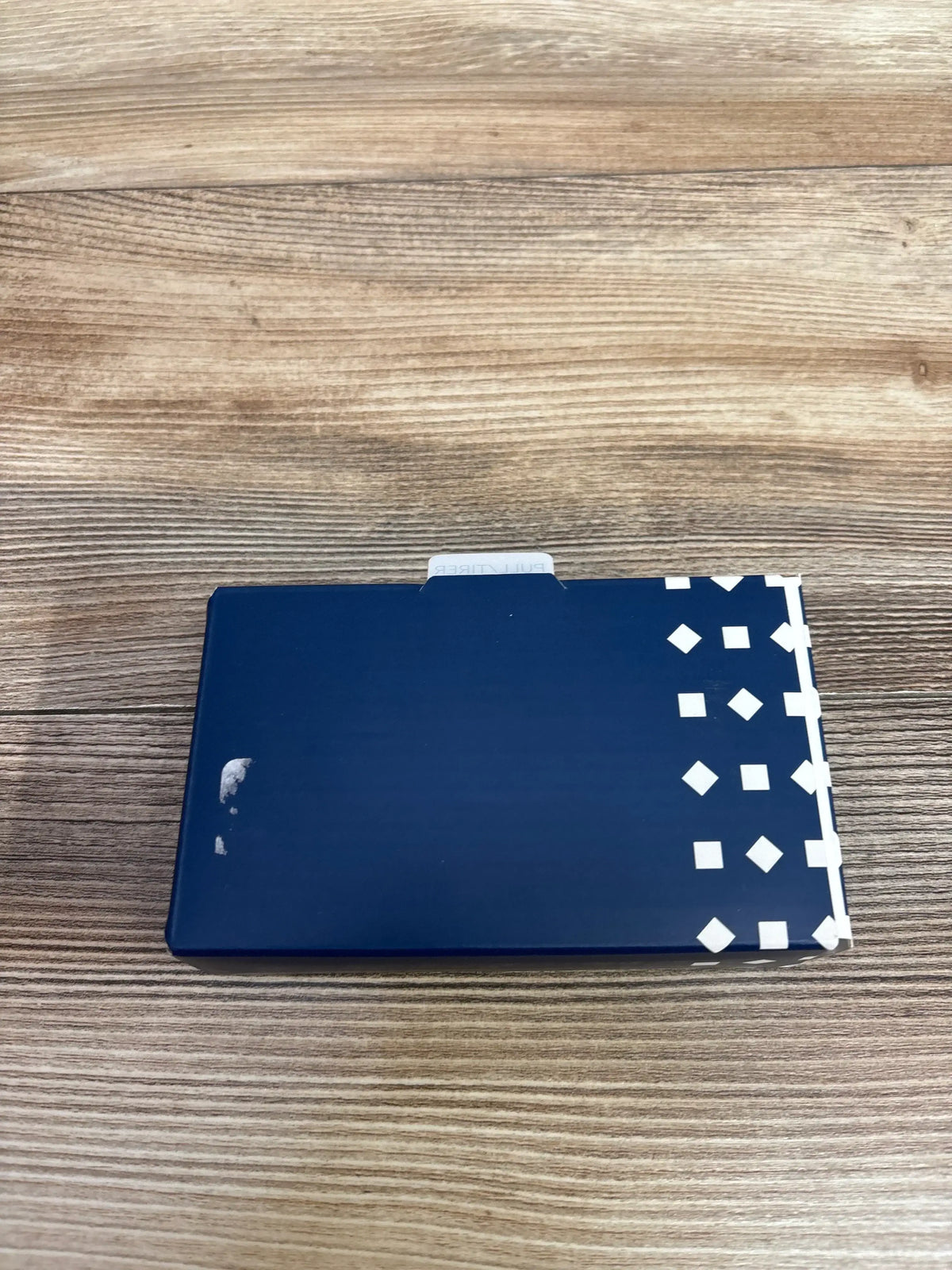 Top-down view of Nanit Breathing Band Wrap (0–3M) box showing navy packaging with white geometric pattern on a wooden surface