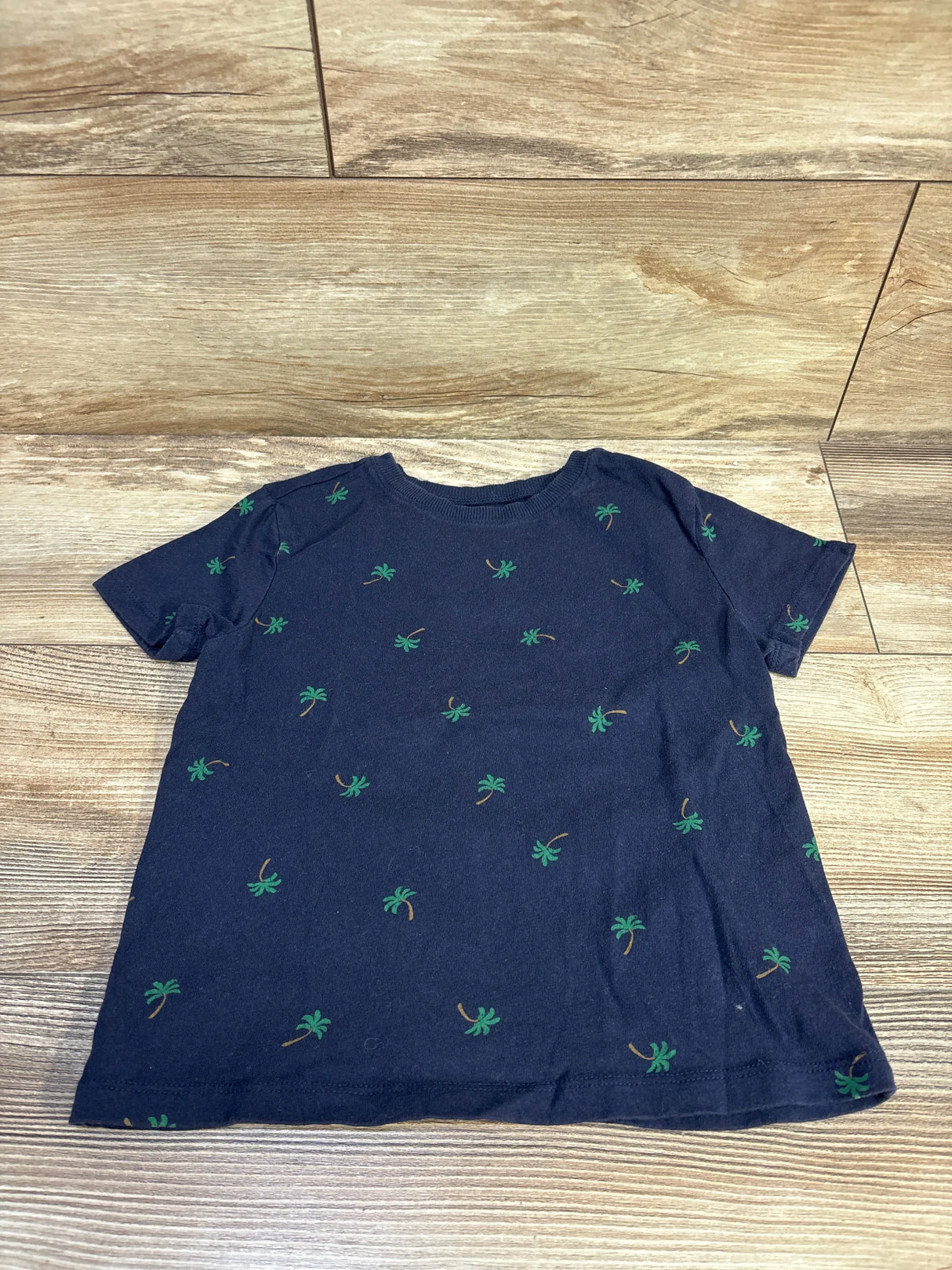 Flat lay of navy Old Navy toddler short-sleeve T-shirt showing small green palm tree all-over print on wood floor background