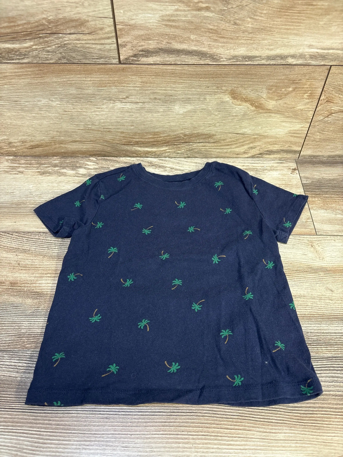 Flat lay of navy Old Navy toddler short-sleeve T-shirt showing small green palm tree all-over print on wood floor background