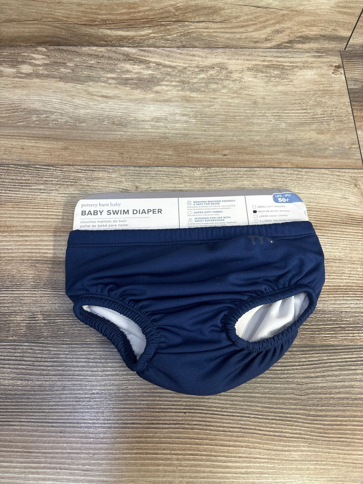 Front view of navy Pottery Barn Baby swim diaper size Medium 12m showcasing elastic leg openings and white inner lining on wood floor background