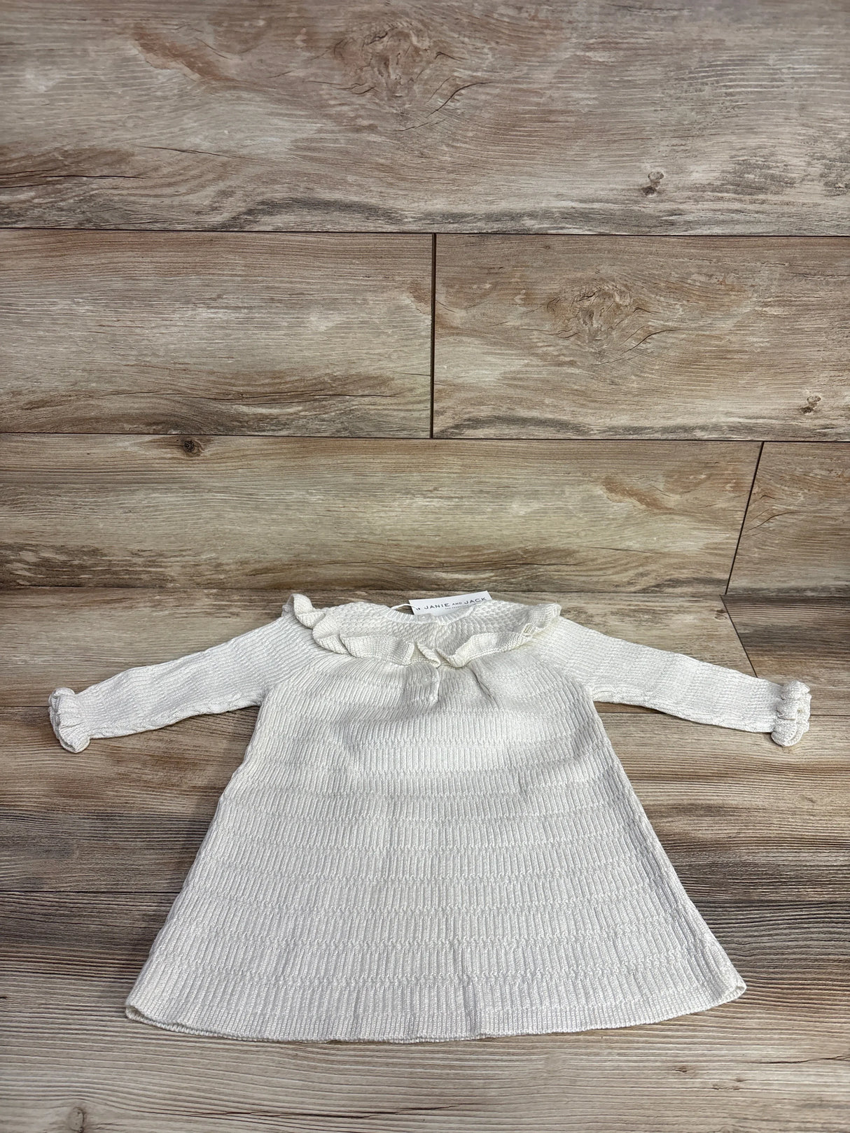 Cream long-sleeve toddler dress with ruffled collar and cuffs on wooden surface