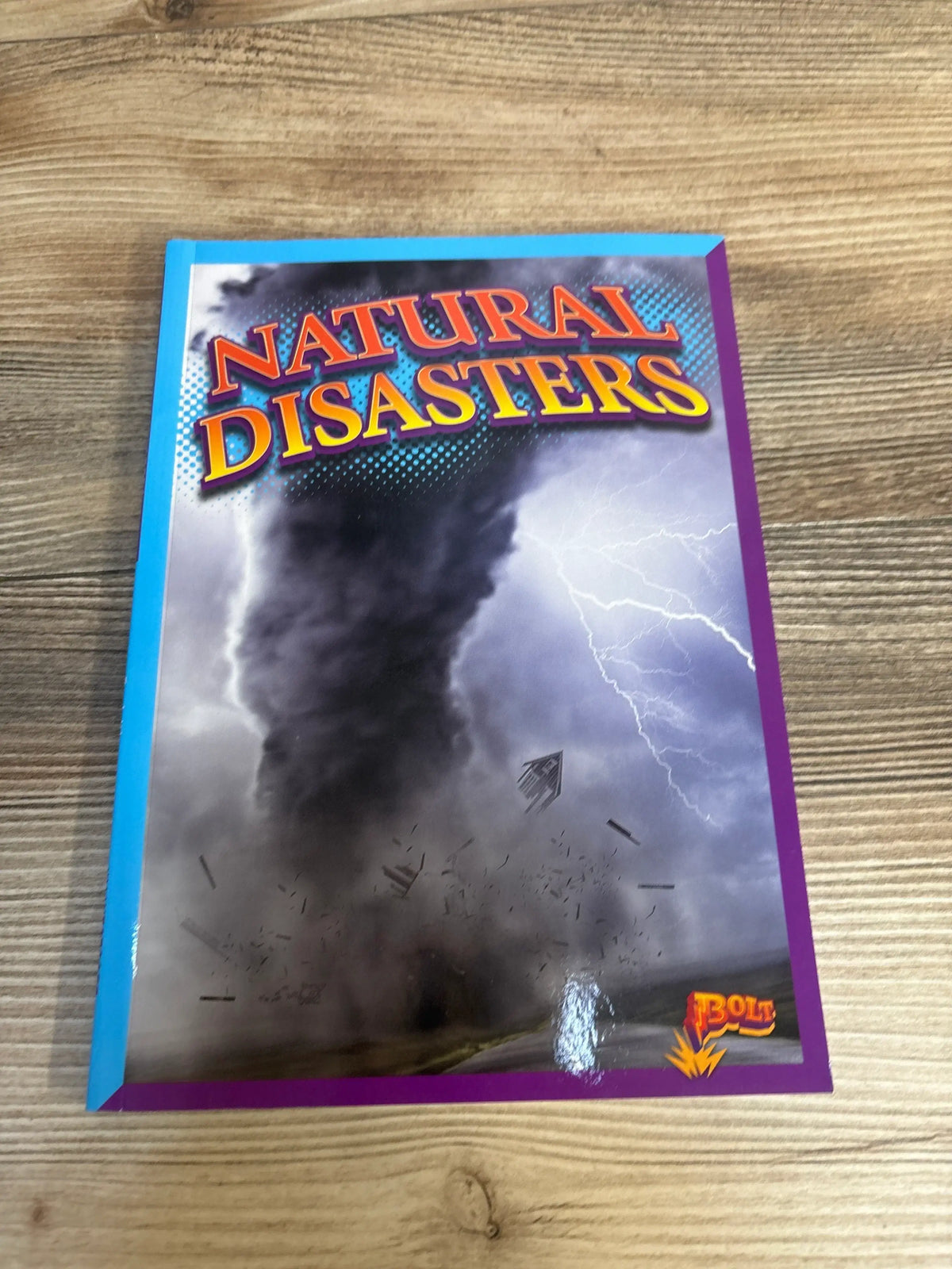 Front cover of Natural Disasters paperback children’s book showcasing a tornado and lightning illustration with wood table background