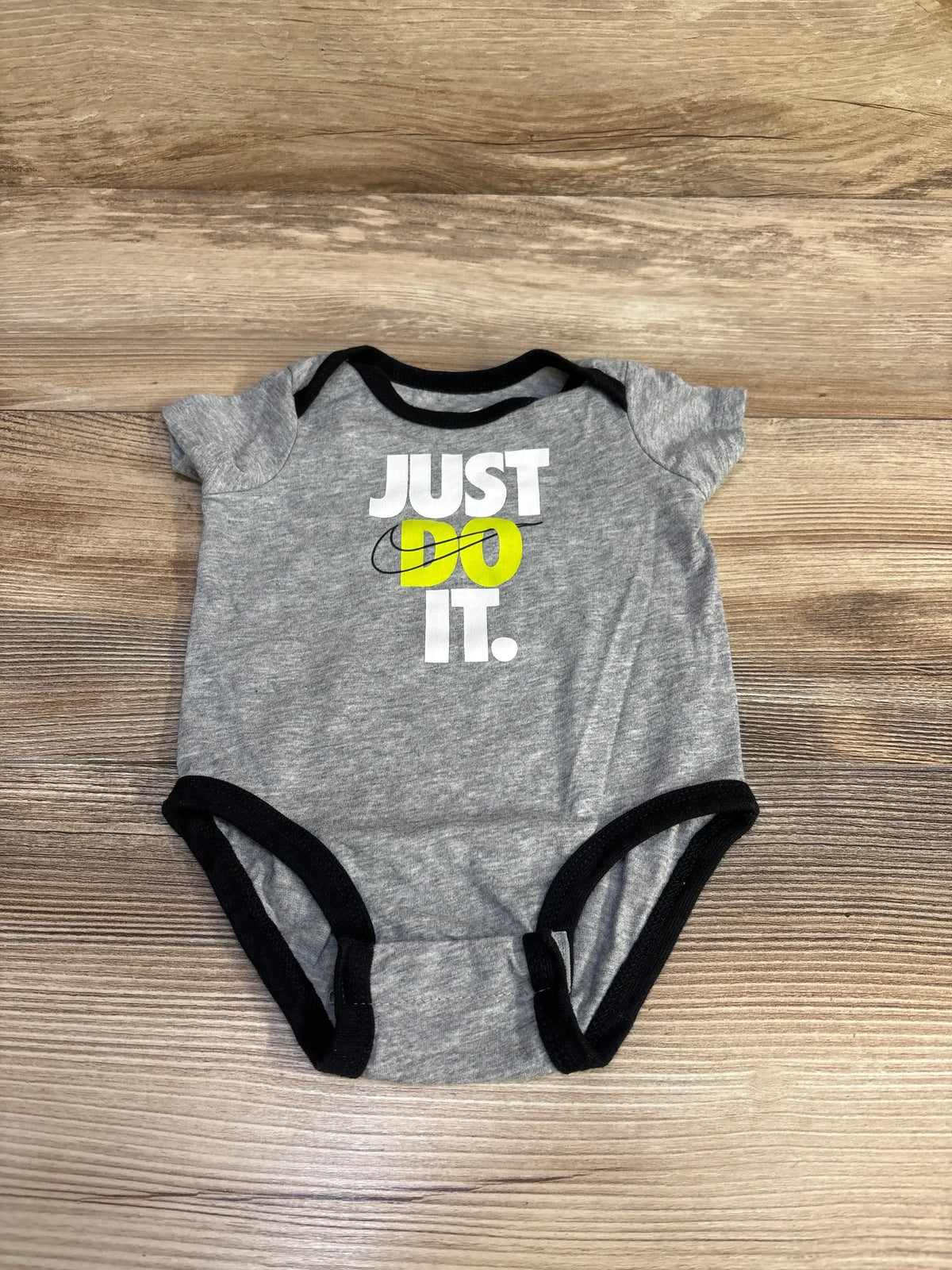 Top-down of grey Nike bodysuit (3M) showing JUST DO IT print with yellow DO and black trim on wood background