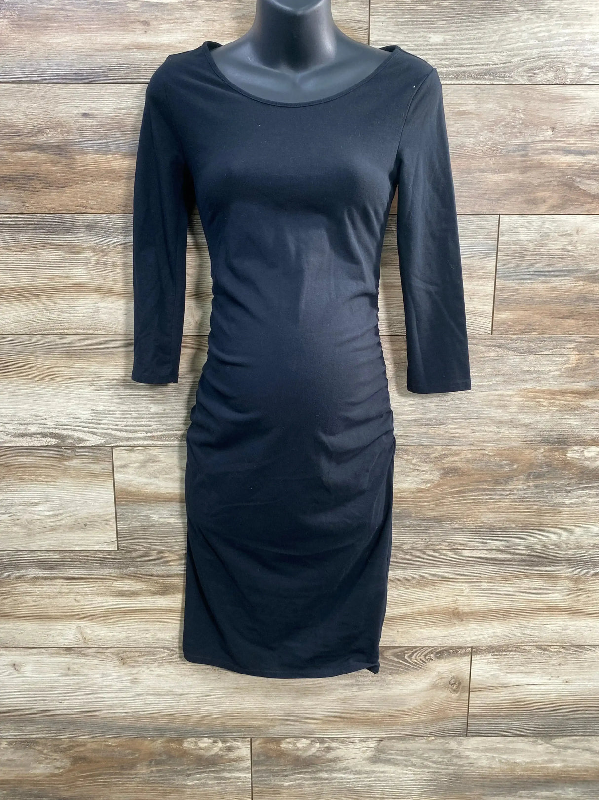 Front view of Isabel maternity black bodycon dress with ruched sides and three-quarter sleeves against wood background