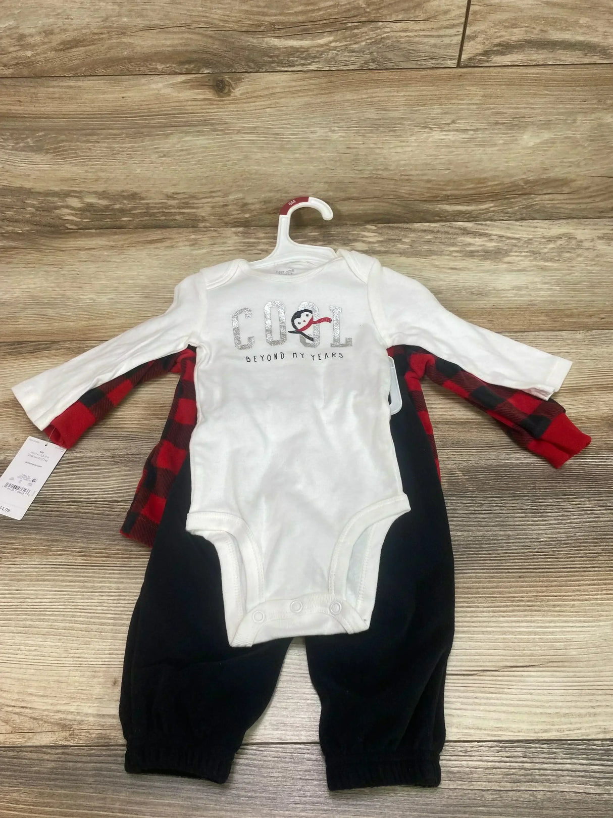 Front view of size 6M 3-piece set, white onesie with glitter COOL penguin, red buffalo-plaid top and black pants on wood